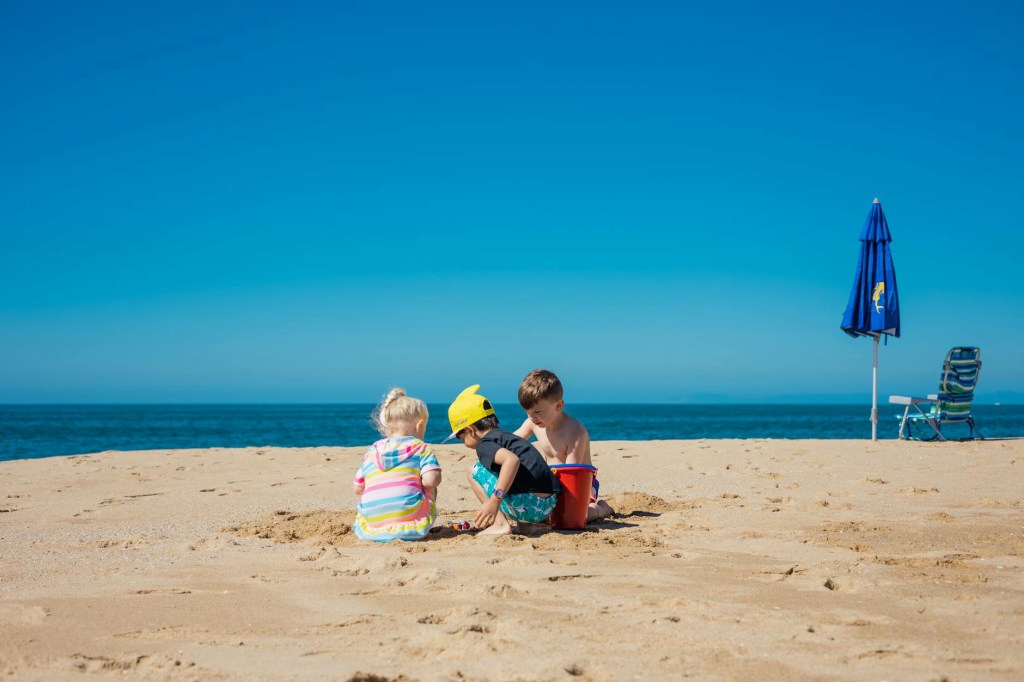 Image of twins and a toddler playing in the sand at the beach. 